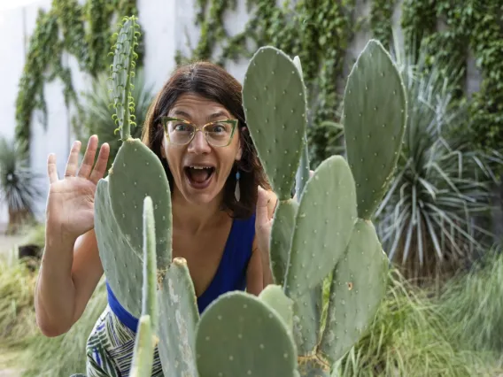 Image of Elise Gornish smiling and raising hand behind a cactus