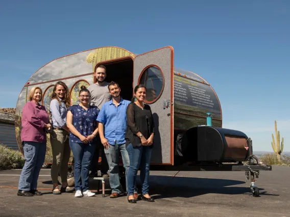 Researchers stand in front of a camper painted with desert scenes